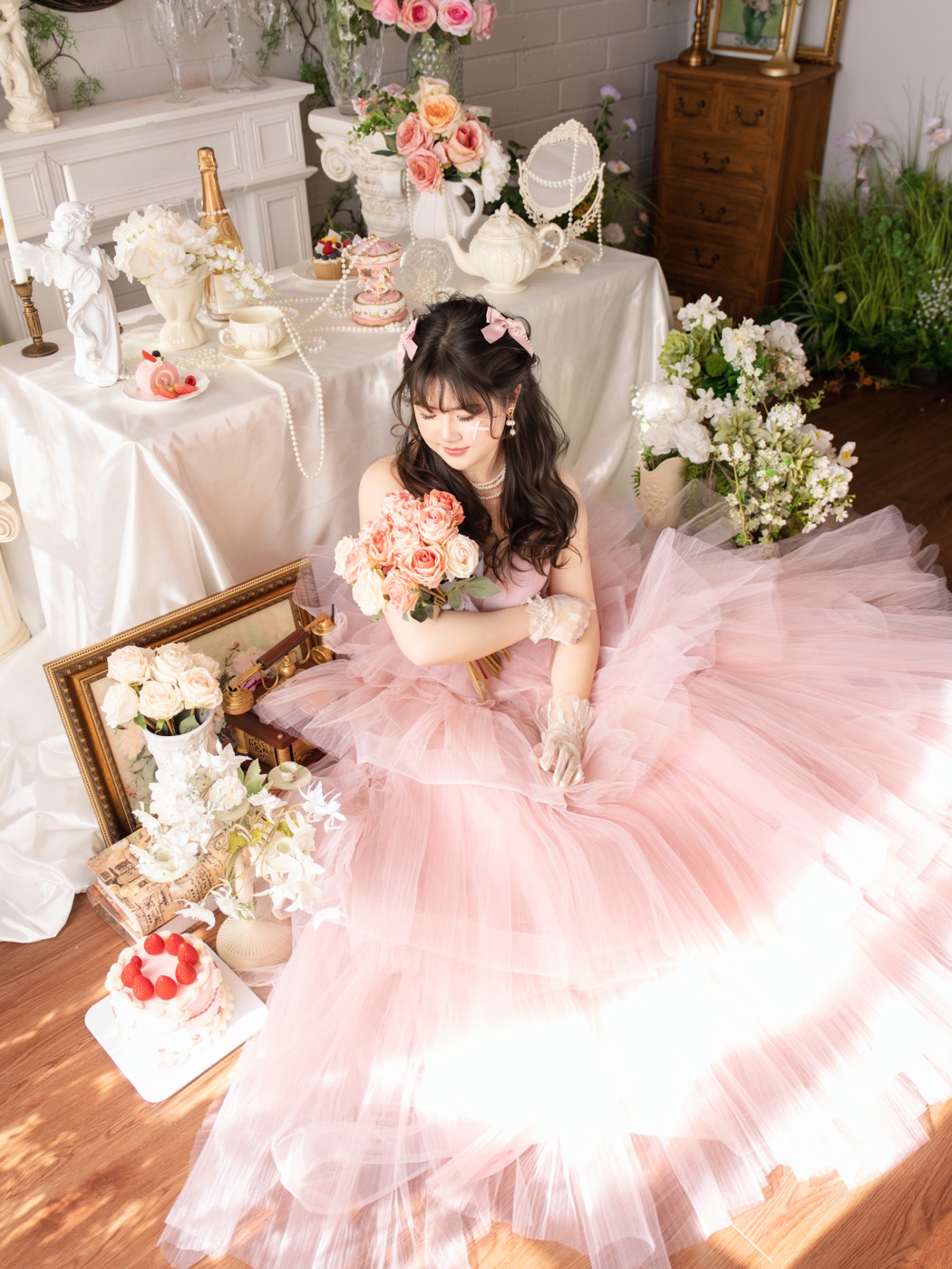 The artist behind Liyko in a soft pink tulle dress, holding a bouquet of roses in a dreamy floral setting